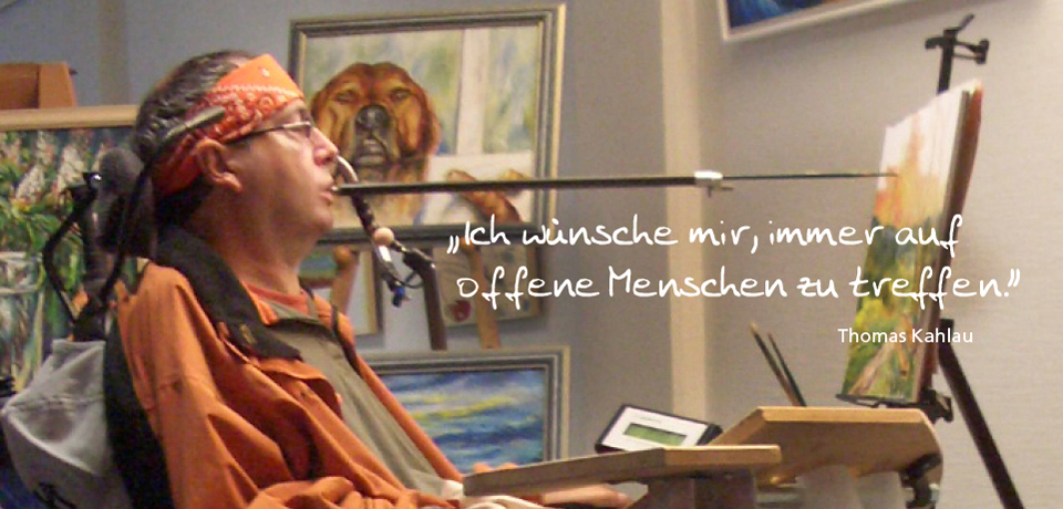 Mann im Rollstuhl mit Pinsel im Mund malt an Staffelei, Gemälde und Hundebild im Hintergrund, Zitat: „Ich wünsche mir, immer auf offene Menschen zu treffen.“ – Thomas Kahlau, barrierefreie Kunst, Inklusion, Künstler.