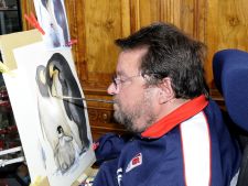 Mann im Rollstuhl malt mit einem Pinsel im Mund ein Bild von Pinguinen auf Papier; barrierefreie Kunst, Kreativität trotz Behinderung, inklusives Kunsterlebnis, Künstler bei der Arbeit, inspirierende Tiermalerei, detailreiches Bild.