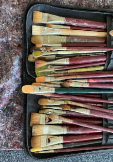 Verschiedene Künstlerpinsel mit roten Holzgriffen und hellen Borsten liegen ordentlich in einem schwarzen Etui auf grauem Untergrund, ideal für Malerei, Kunstbedarf, Hobby, hochwertiges Pinselset für Acryl und Öl.