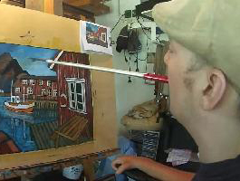 Mann mit Mütze malt mit einem im Mund gehaltenen Pinsel ein farbenfrohes Bild eines Hafens mit Boot und Häusern auf einer Leinwand, barrierefreie Kunst für Menschen mit Behinderung, inklusives Malen, Kreativität ohne Einschränkung.